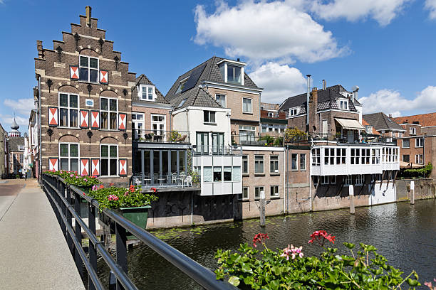 Charming traditional Dutch houses line the historic canal in Gorinchem, adorned with balconies and reflective waters, under a bright blue sky.